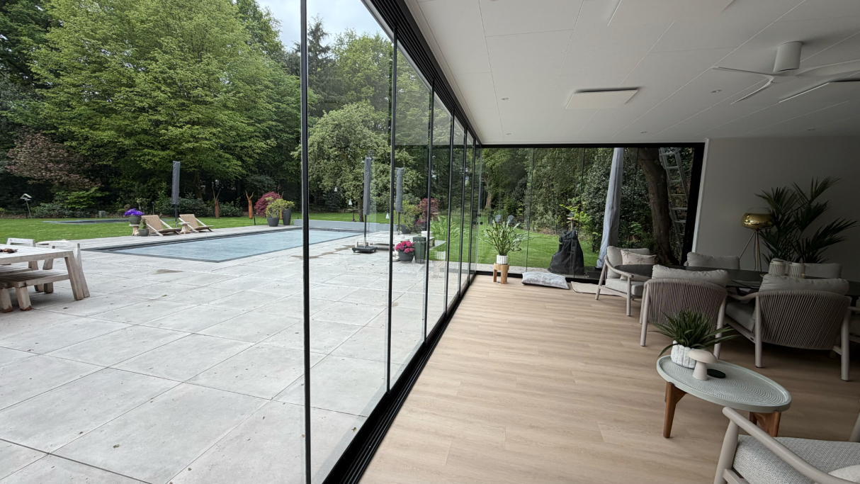 Binnenruimte van het poolhouse met grote glaspartijen en uitzicht op het terras, het zwembad en de tuin.